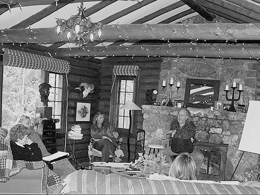 Phil Lawson leading a session by the stone fireplace in the log cabin, with participants gathered around