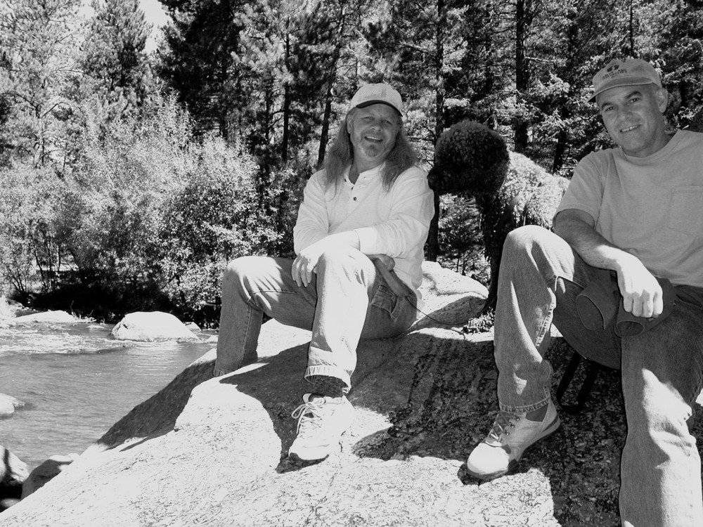 Phil Lawson and Robert L. Lindstrom sitting on a boulder beside a mountain creek, with a dog between them